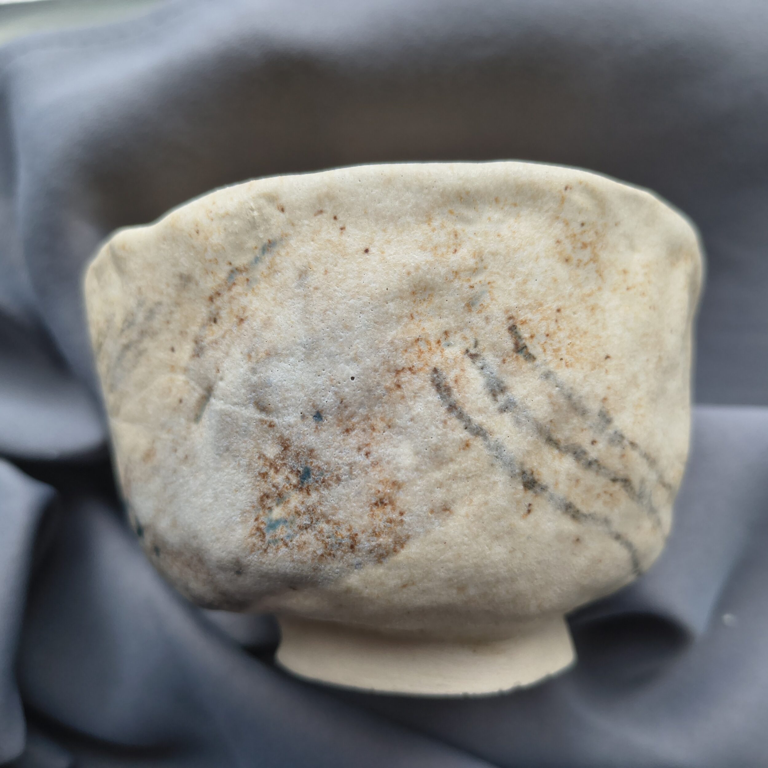 A handmade ceramic bowl with beige glaze and brown speckles sits on a gray surface. The bowl is