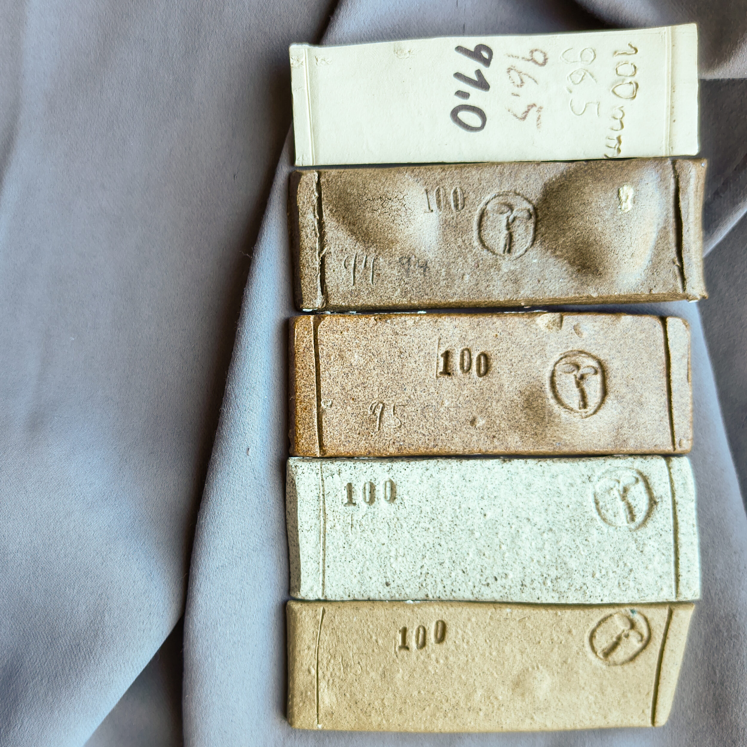 Mehrere rechteckige Keramiksteine mit der Zahl 100 und Herstellerlogo gestapelt auf weißem Untergrund. Oben liegt ein handges